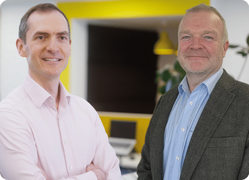 Two men standing in an office. Description generated by AI