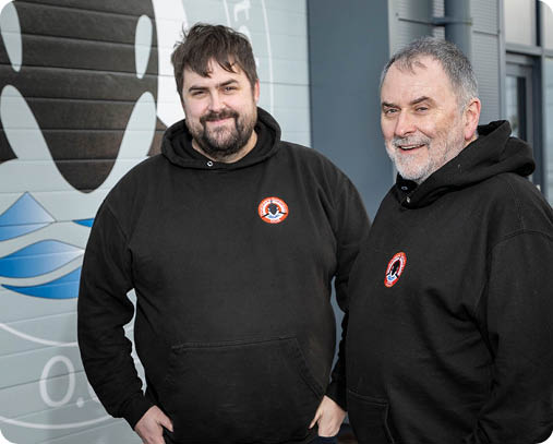 Two men wearing black hoodies. Description generated by AI