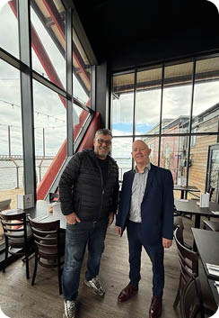 Two men standing in a restaurant. Description generated by AI